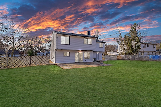 back of house at dusk featuring a fenced backyard, a chimney, a patio, and a yard