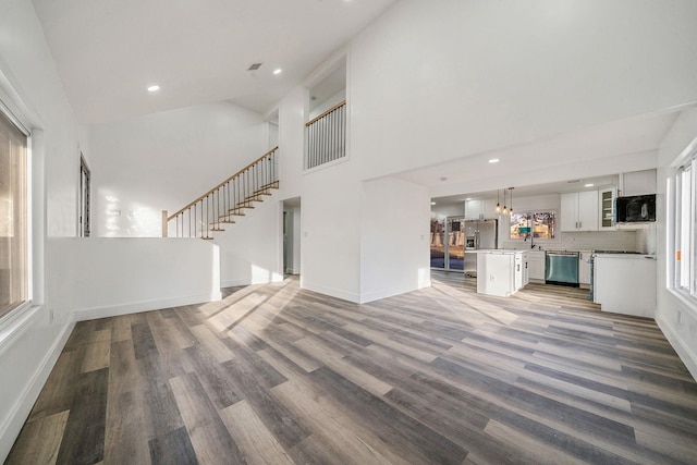 unfurnished living room featuring baseboards, stairs, a towering ceiling, and wood finished floors