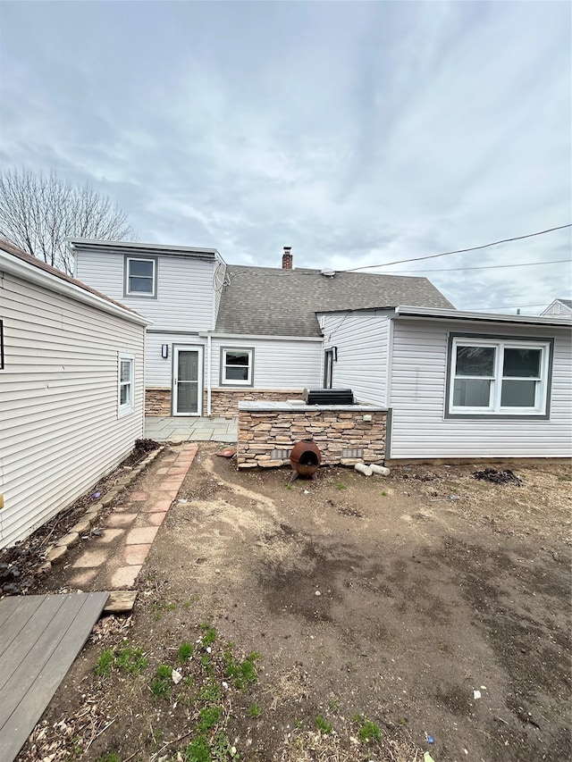 22 Peacock Ln, Levittown, NY 11756 - rear view of house with a chimney, a shingled roof, and stone siding