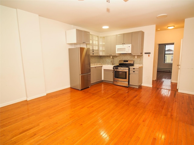 kitchen featuring appliances with stainless steel finishes, a baseboard heating unit, light countertops, decorative backsplash, and glass insert cabinets