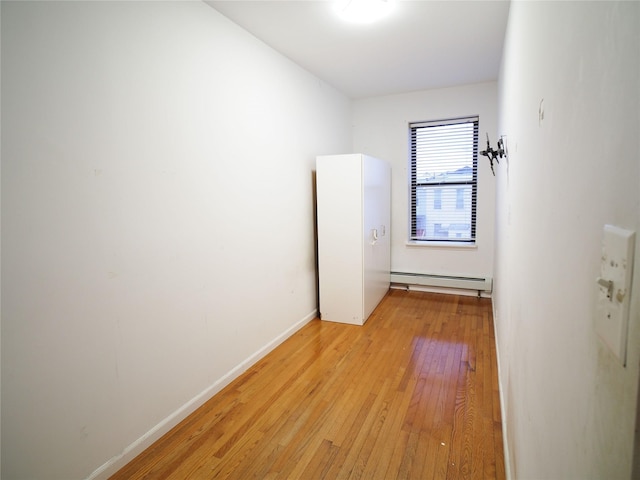 empty room featuring baseboard heating, light wood-style flooring, and baseboards