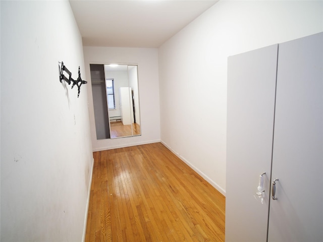 corridor with light wood-style flooring, baseboards, and a baseboard heating unit