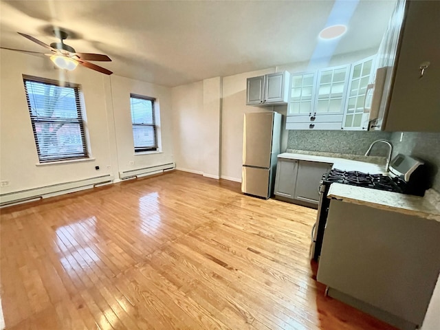 kitchen featuring appliances with stainless steel finishes, a baseboard heating unit, gray cabinets, light wood-style floors, and light countertops