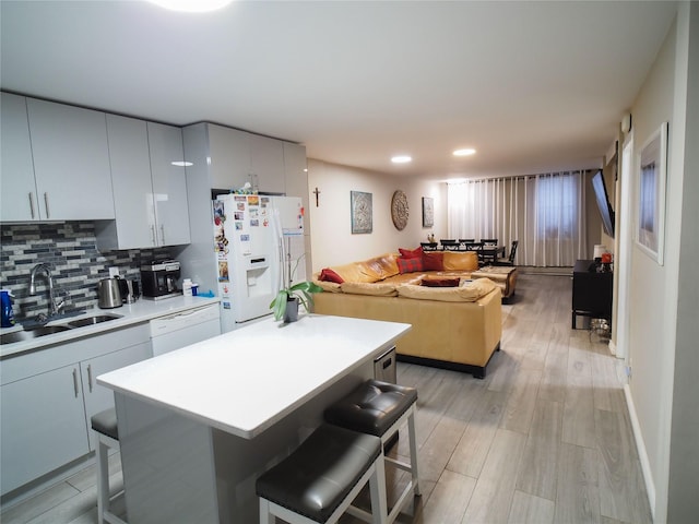 kitchen with a sink, a kitchen breakfast bar, white appliances, open floor plan, and recessed lighting