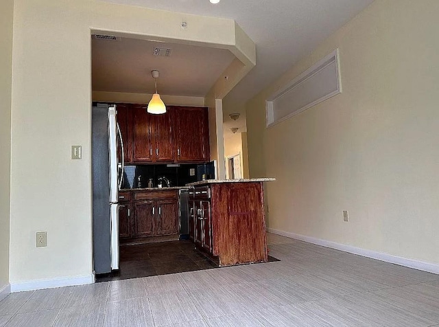 kitchen featuring freestanding refrigerator, baseboards, a peninsula, backsplash, and decorative light fixtures