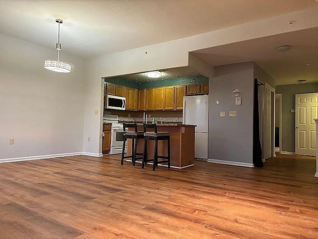 kitchen with stainless steel gas stove, freestanding refrigerator, dark wood-type flooring, brown cabinets, and baseboards