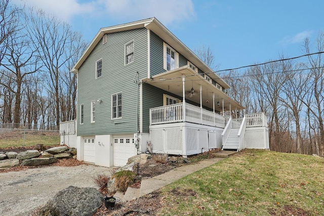 view of front of house with an attached garage, a front lawn, dirt driveway, ceiling fan, and stairway