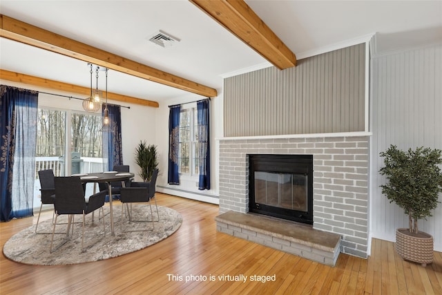 living area featuring a baseboard heating unit, hardwood / wood-style flooring, beam ceiling, and a brick fireplace