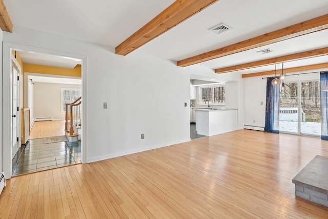 unfurnished living room featuring a baseboard radiator, light wood finished floors, and a wealth of natural light