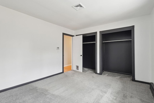 unfurnished bedroom featuring light colored carpet, baseboard heating, two closets, baseboards, and visible vents