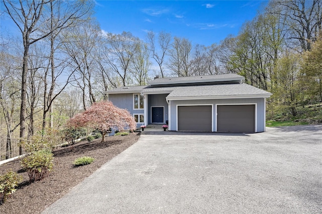 view of front facade with roof with shingles, an attached garage, and aphalt driveway