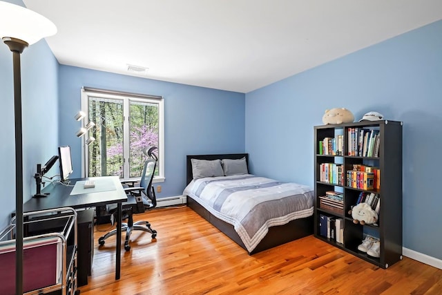 bedroom with baseboards, baseboard heating, wood finished floors, and visible vents