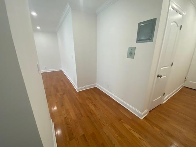 hallway featuring crown molding, baseboards, wood finished floors, and electric panel