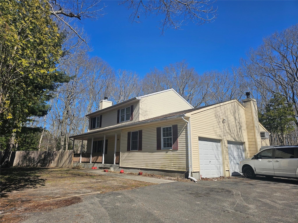 view of front of house with aphalt driveway, fence, a chimney, an attached garage, and covered porch