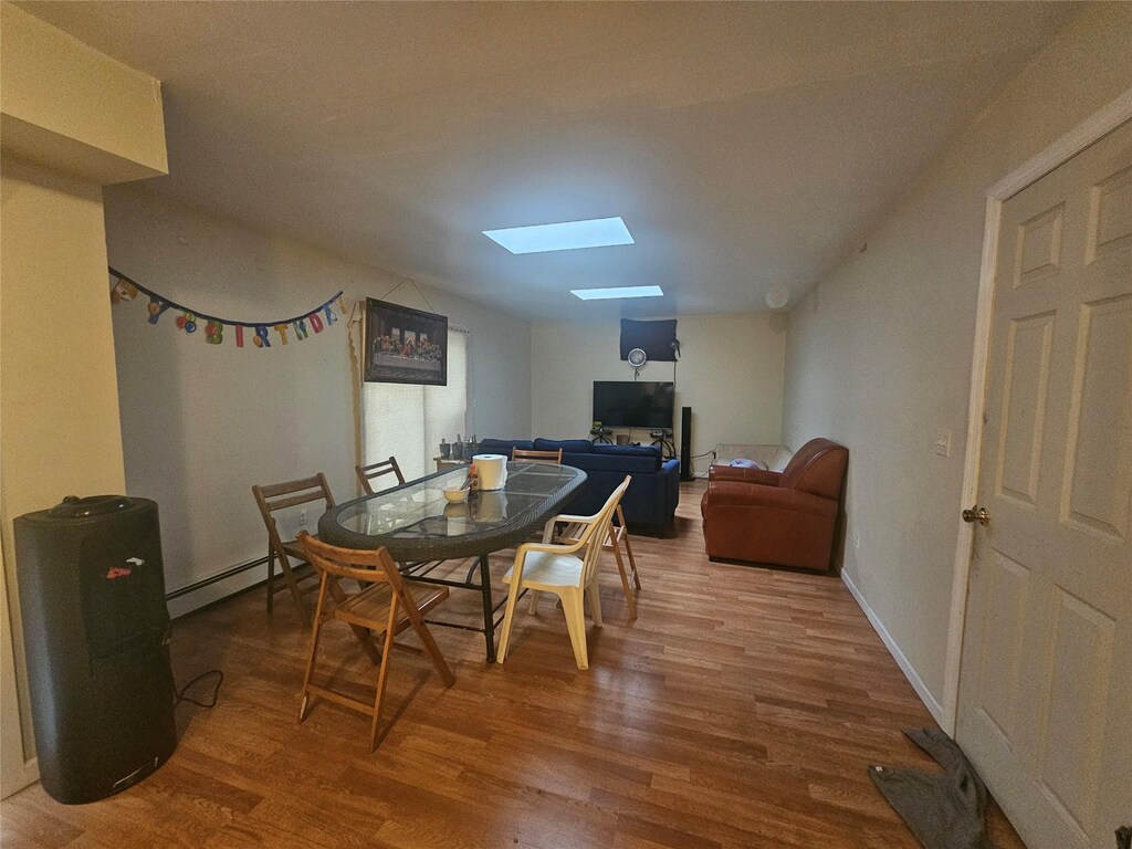 dining space with a baseboard radiator, a skylight, baseboards, and wood finished floors
