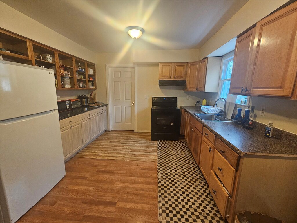 kitchen with light wood finished floors, dark countertops, black / electric stove, a sink, and freestanding refrigerator