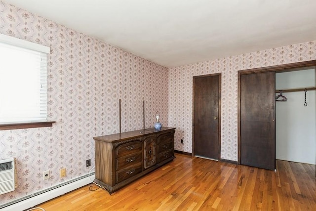 unfurnished bedroom with multiple closets, baseboard heating, wallpapered walls, and light wood-style flooring