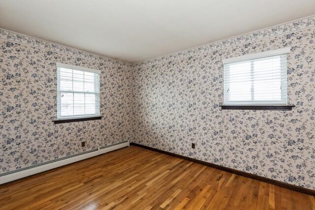 empty room with a wealth of natural light, baseboard heating, and wood finished floors