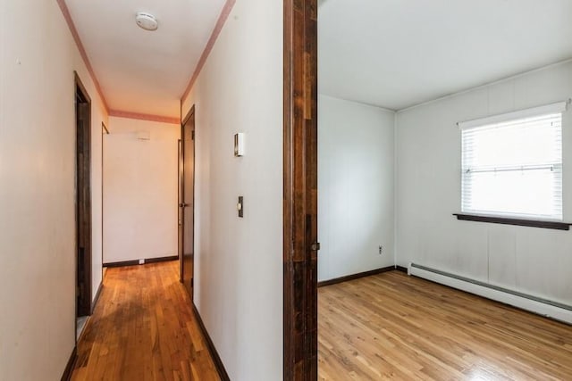 corridor with a baseboard radiator, baseboards, ornamental molding, and light wood-type flooring