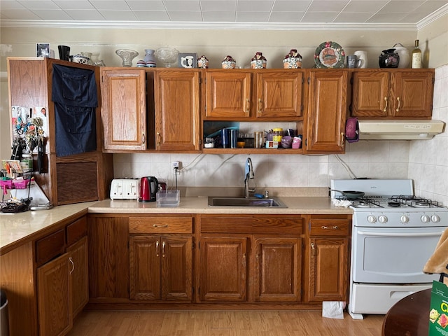 kitchen with a sink, white range with gas cooktop, brown cabinets, and under cabinet range hood
