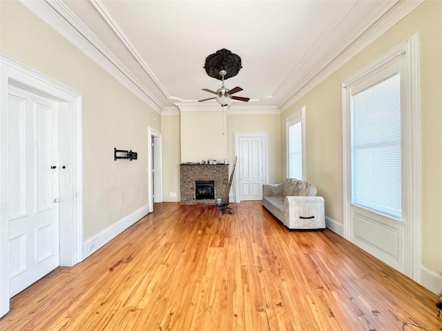unfurnished room featuring baseboards, a fireplace, light wood-style flooring, crown molding, and ceiling fan
