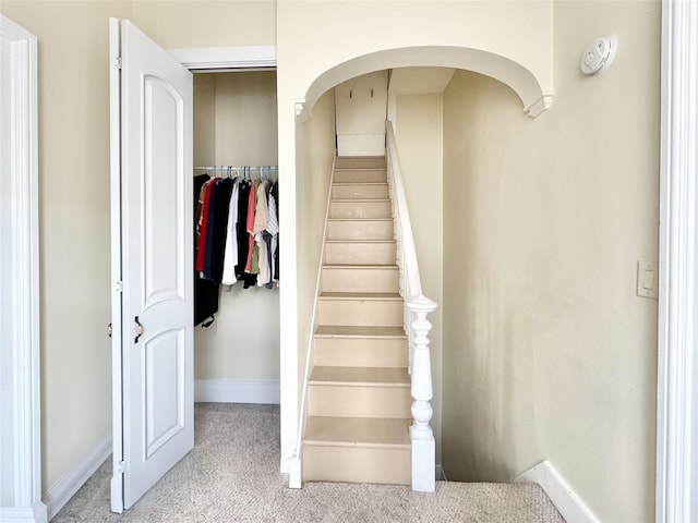 stairway featuring arched walkways, baseboards, and carpet floors
