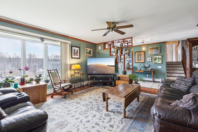 living area with ceiling fan, ornamental molding, stairway, wood finished floors, and baseboards