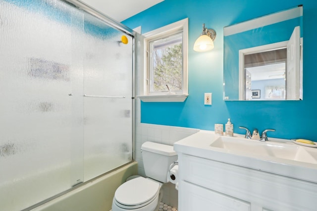 bathroom with vanity, a wainscoted wall, toilet, enclosed tub / shower combo, and tile walls