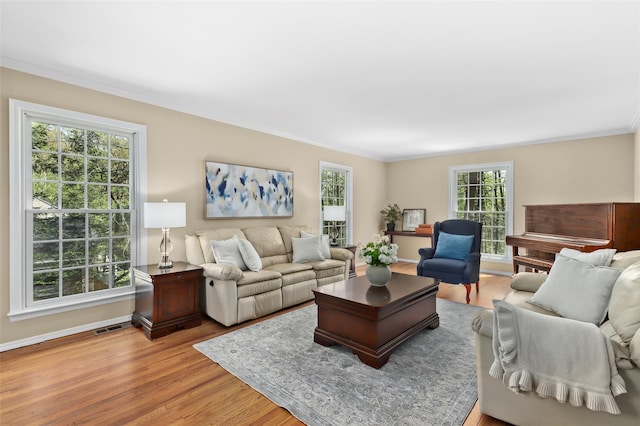 living area with crown molding, baseboards, visible vents, and light wood-type flooring