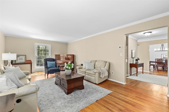 living room with baseboards, an inviting chandelier, ornamental molding, and light wood-style floors