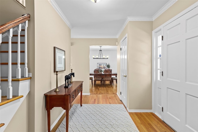 foyer entrance featuring ornamental molding, stairs, baseboards, a chandelier, and light wood finished floors