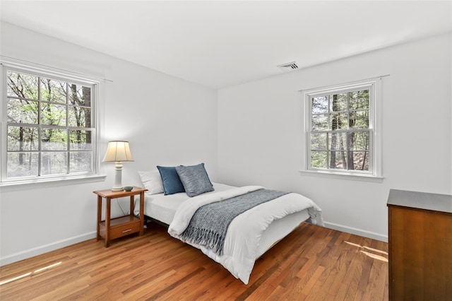 bedroom with baseboards, visible vents, and wood finished floors