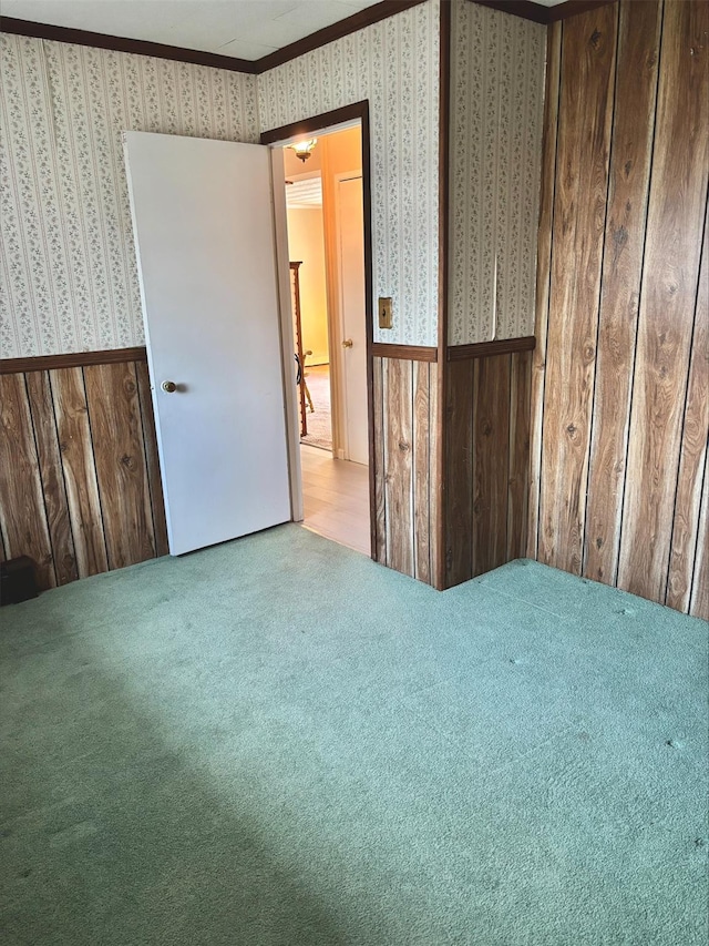 carpeted spare room with wood walls, crown molding, a wainscoted wall, and wallpapered walls