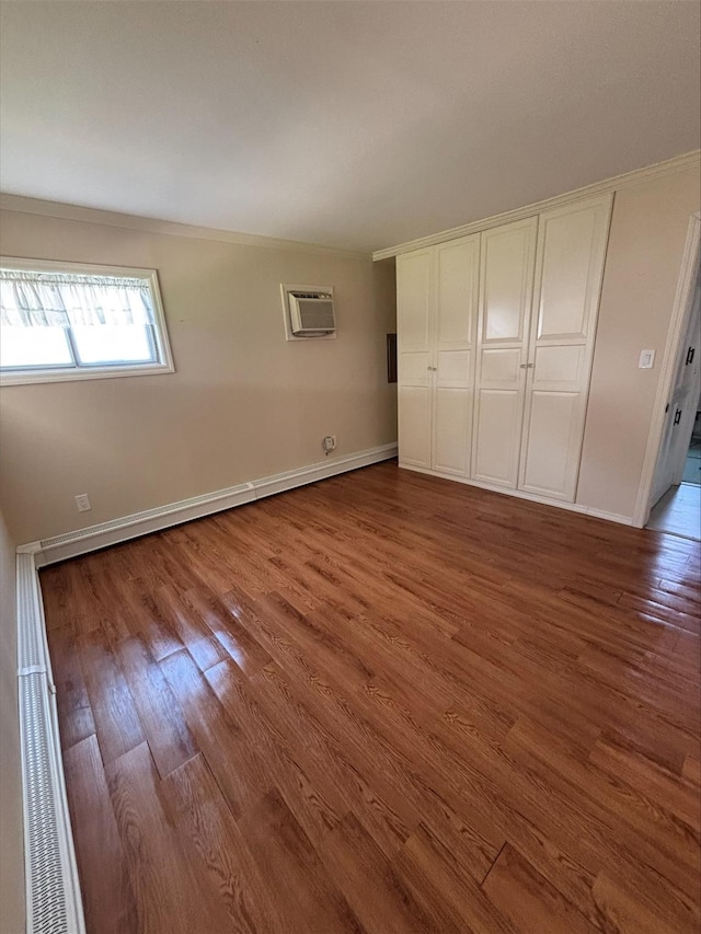 unfurnished bedroom with crown molding, wood finished floors, an AC wall unit, and baseboards