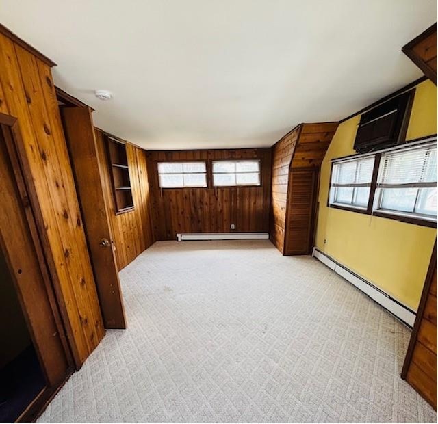 interior space featuring light colored carpet, a baseboard radiator, baseboards, and wooden walls