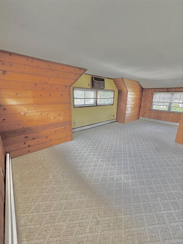additional living space featuring a baseboard heating unit, wood walls, carpet, and a healthy amount of sunlight
