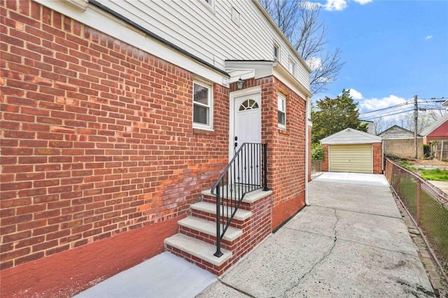 doorway to property with a detached garage, fence, and brick siding
