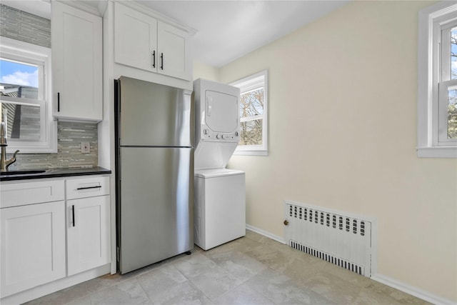 laundry room featuring stacked washing maching and dryer, radiator heating unit, a sink, and baseboards