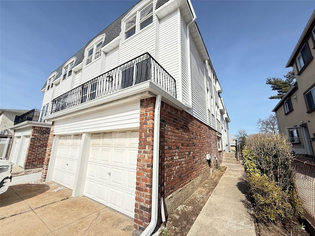 view of property exterior featuring brick siding, concrete driveway, a balcony, and an attached garage