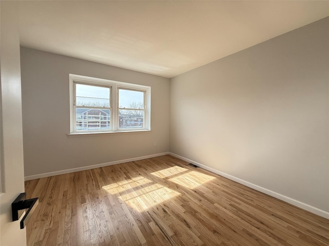 spare room with baseboards, visible vents, and wood finished floors