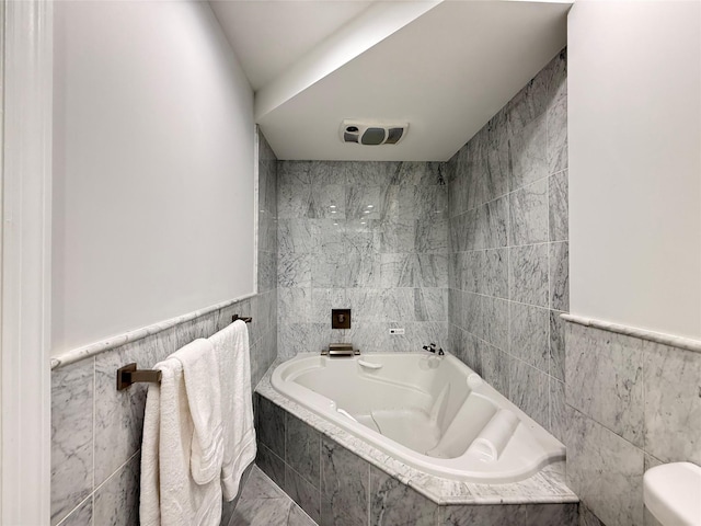 full bath featuring tiled bath, tile walls, and visible vents
