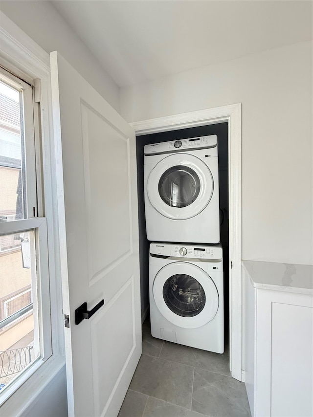 washroom with tile patterned floors, stacked washer and clothes dryer, a healthy amount of sunlight, and laundry area