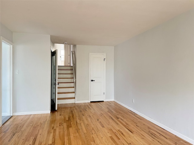 spare room featuring baseboards, stairway, and light wood-type flooring