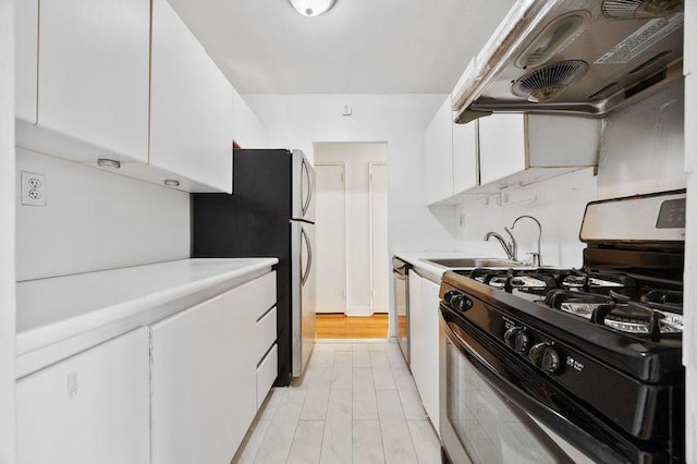 kitchen featuring appliances with stainless steel finishes, light countertops, a sink, ventilation hood, and white cabinets