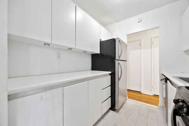 kitchen with light countertops, freestanding refrigerator, white cabinetry, and range