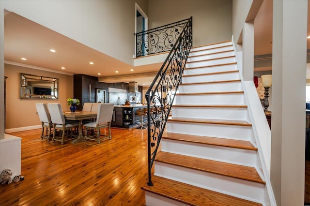 stairway with hardwood / wood-style flooring, a towering ceiling, recessed lighting, and ornamental molding