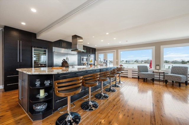 kitchen with light wood finished floors, island range hood, built in refrigerator, open shelves, and built in fridge