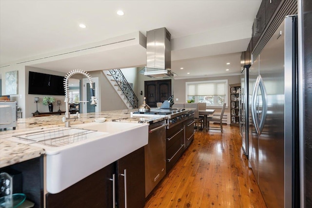 kitchen featuring light wood finished floors, dark brown cabinets, open floor plan, island range hood, and appliances with stainless steel finishes