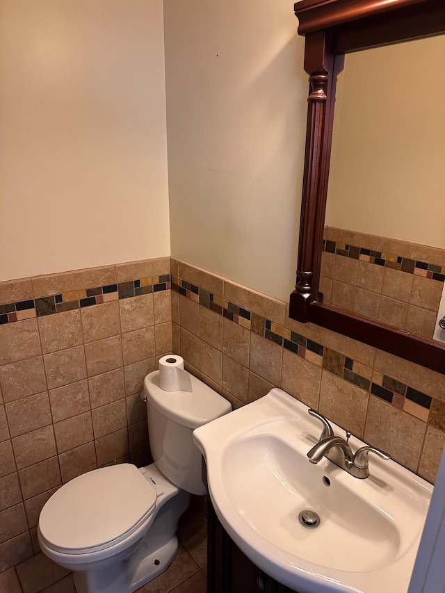 half bath with tile walls, a wainscoted wall, a sink, and toilet
