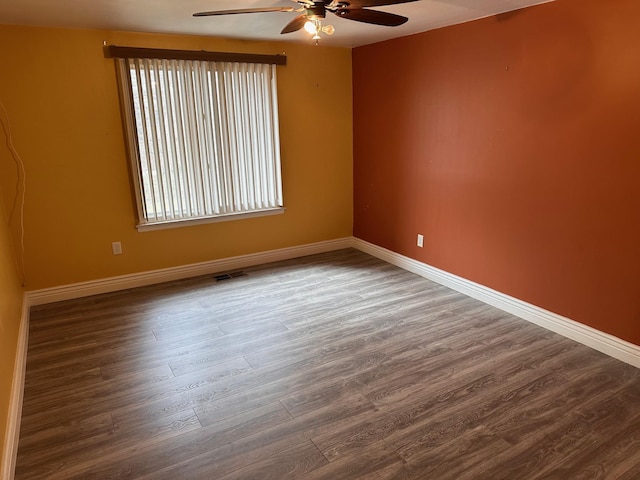 empty room with wood finished floors, baseboards, a ceiling fan, and visible vents